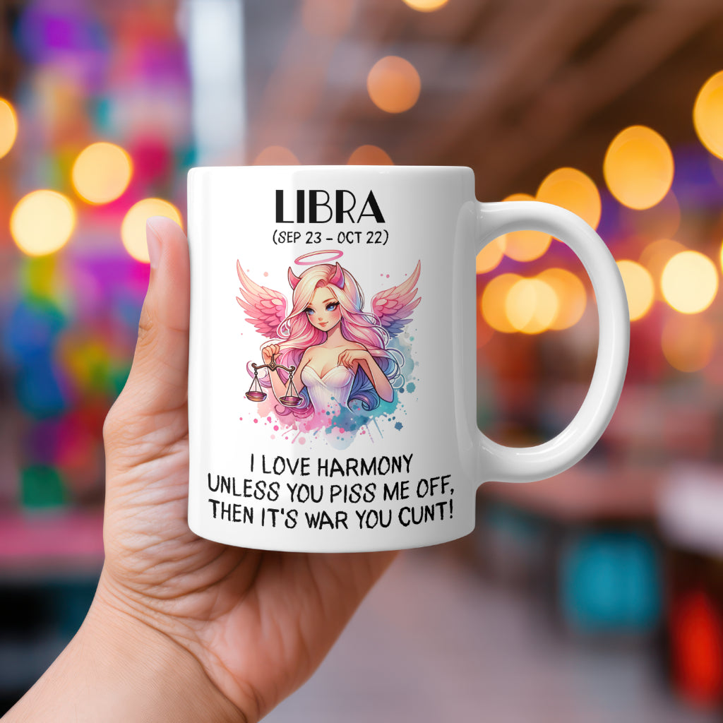 A white 11oz coffee mug featuring a bold Libra-themed design. The artwork showcases a pink-haired angelic figure with devil horns, holding the Libra scales, with soft pastel wings and a dreamy colour palette. Below, the sassy text reads: "I love harmony unless you piss me off, then it's war you cunt!" A cheeky, rude astrology gift for Libra star sign lovers.