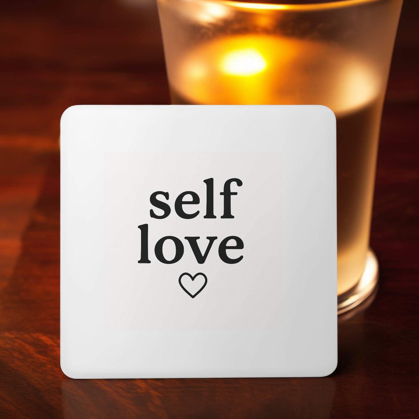 Square white MDF coaster measuring 9cm with "self love" and a heart printed in black text. Designed to complement mugs or add a calming touch to your workspace.