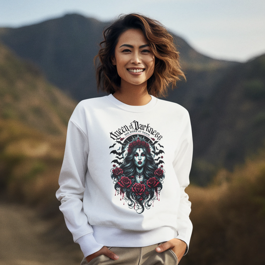 A stylish unisex white sweatshirt featuring a detailed gothic 'Queen of Darkness' graphic with an elegantly imposing female figure surrounded by black and red roses, ornate gothic jewelry, and dark winged motifs, emphasized by a stark black inner collar and cuffs. The design prominently includes the phrase "Queen of Darkness" arched above and "She Rides at Dawn" below, encapsulating a blend of dark fantasy and edgy fashion.