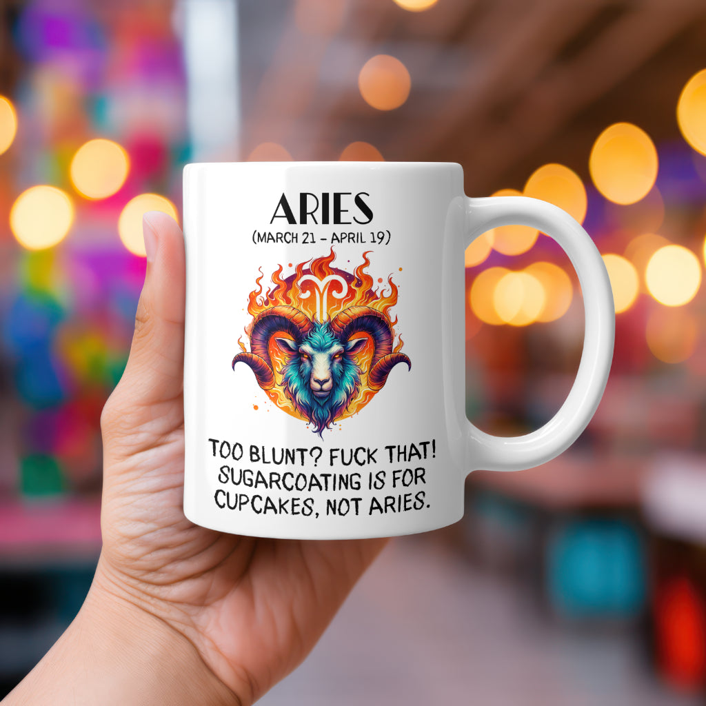 A white 11oz coffee mug featuring a bold Aries-themed design. The artwork showcases a fierce ram’s head engulfed in flames, with the Aries zodiac symbol glowing above it. The fiery colour palette reflects Aries' passionate and direct personality. Below, the sassy text reads: "Too blunt? Fuck that! Sugarcoating is for cupcakes, not Aries." A cheeky, rude astrology gift for Aries star sign lovers.