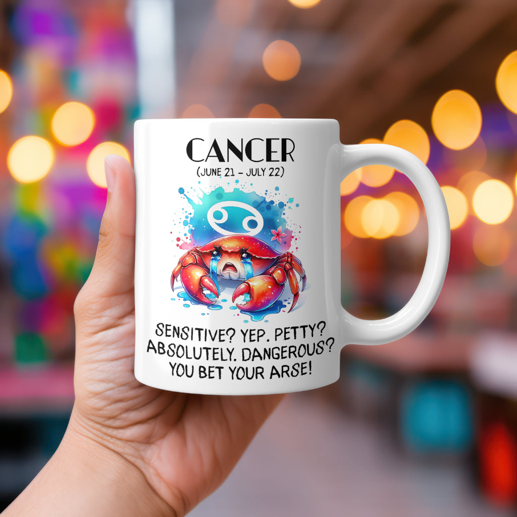 A white 11oz coffee mug featuring a bold Cancer-themed design. The artwork showcases a dramatic crab with teary eyes, clutching its claws menacingly, with the Cancer zodiac symbol glowing in the background. The colours are vibrant and playful. Below, the sassy text reads: "Sensitive? Yep. Petty? Absolutely. Dangerous? You bet your arse!" A cheeky, rude astrology gift for Cancer star sign lovers.