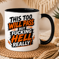 White ceramic funny quote mug featuring the phrase “This Too Will Pass But Fucking Hell Really” in bold black and orange typography. Displayed in a cosy boho-style setting with neutral décor and soft lighting. Available in multiple inner and handle colour options including black, pink, blue, red and yellow.
