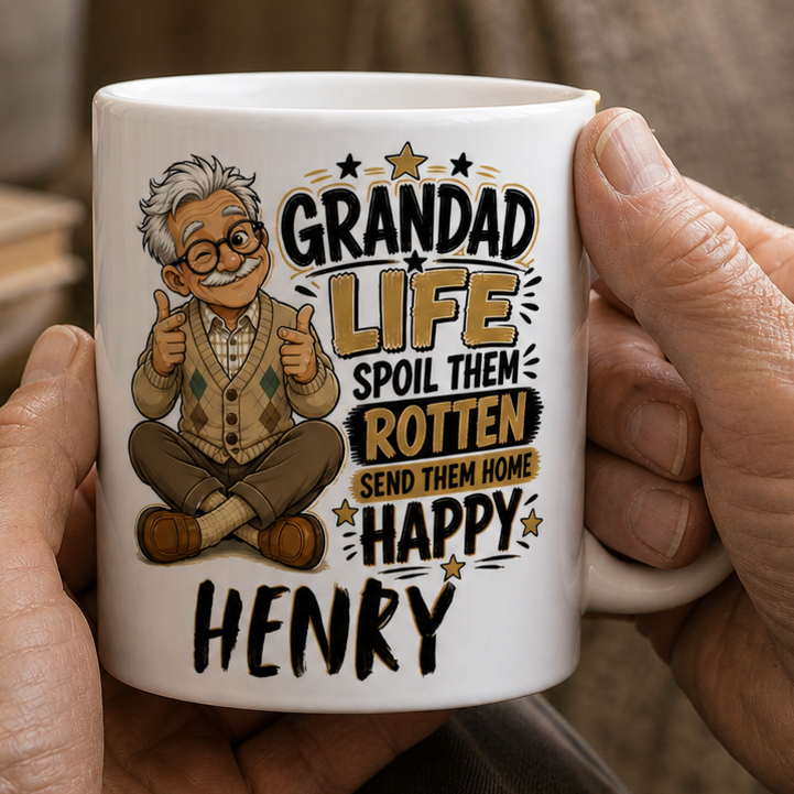 Person holding a mug with a cartoon grandad design and text in a cozy indoor setting.