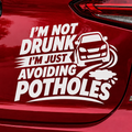 Red car with a humorous decal on the back. I'm not drunk I'm just avoiding potholes funny vinyl decal car sticker.