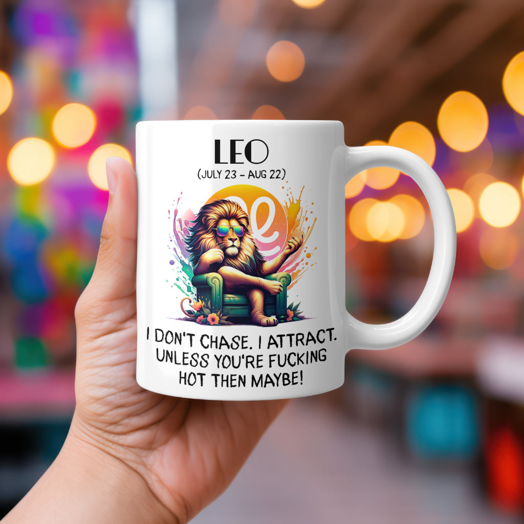 A white 11oz coffee mug featuring a bold Leo-themed design. The artwork showcases a majestic lion lounging in a green armchair, wearing stylish sunglasses and exuding confidence, with a vibrant Leo zodiac symbol in the background. Below, the sassy text reads: "I don’t chase. I attract. Unless you're fucking hot, then maybe!" A cheeky, rude astrology gift for Leo star sign lovers.