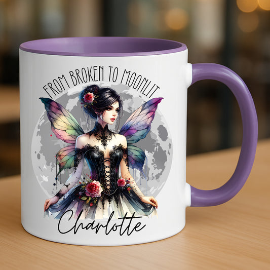Mug with gothic fairy and moon design and text 'From Broken to Moonlit' on a wooden surface. Personalised with any name.
