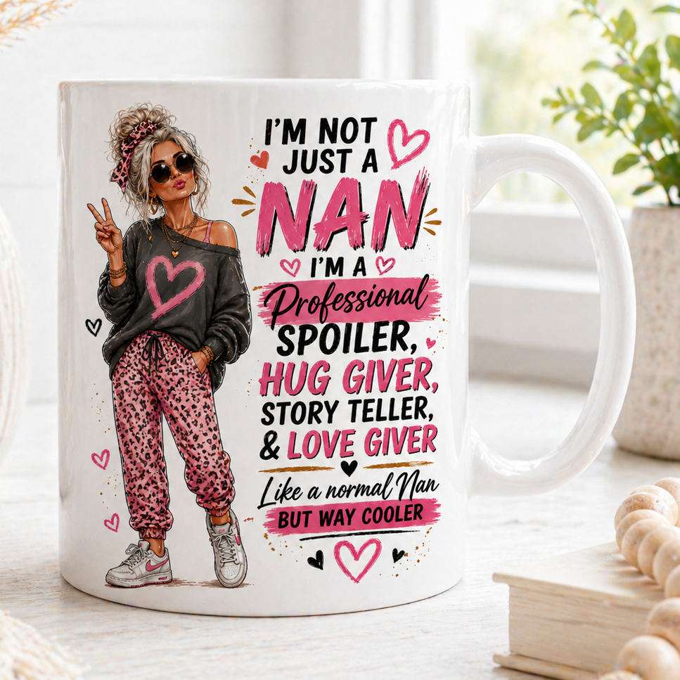 Mug with a design of a nan and text about being a 'Professional Spoiler, Hug Giver, Story Teller, & Love Giver' on a decorative surface.