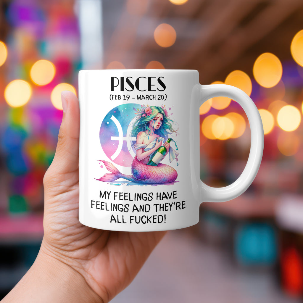 A white 11oz coffee mug featuring a colourful Pisces-themed design. The artwork depicts a mermaid with pastel hair holding a bottle of champagne, set against a glowing Pisces zodiac symbol. Below, the bold text reads: "My feelings have feelings and they're all fucked!" A funny, rude astrology gift for Pisces star sign fans.