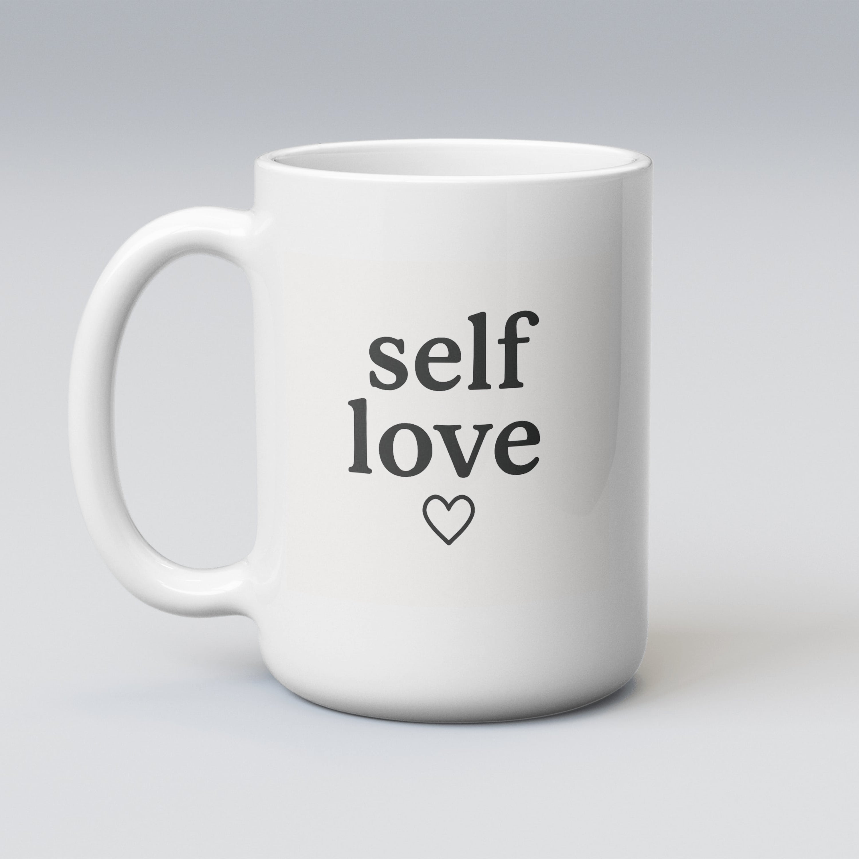 Large white 15oz ceramic mug featuring the phrase "self love" with a heart underneath, printed in sleek black lettering. Perfect for big brews and bold affirmations.