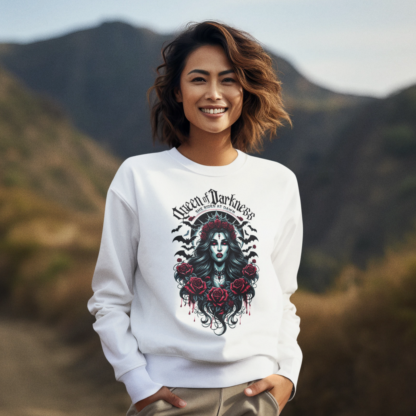 A stylish unisex white sweatshirt featuring a detailed gothic 'Queen of Darkness' graphic with an elegantly imposing female figure surrounded by black and red roses, ornate gothic jewelry, and dark winged motifs, emphasized by a stark black inner collar and cuffs. The design prominently includes the phrase "Queen of Darkness" arched above and "She Rides at Dawn" below, encapsulating a blend of dark fantasy and edgy fashion.